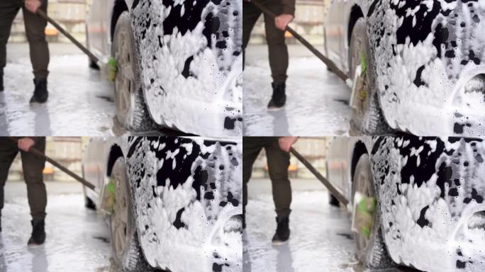 一名男子洗了一辆黑色汽车。在自助洗车场用轮刷清洁轮辋和车轮。汽车服务业。