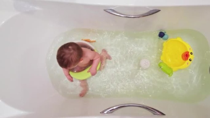 快乐的蹒跚学步的男婴坐在椅子上沐浴在白色的浴缸里。孩子在大浴缸里玩水，孩子九个月大