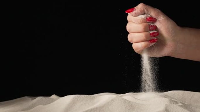 女性的手在孤立的黑色工作室背景上挤压并洒出少量白色干沙。沙粒通过手指筛分。特写纯天然矿物石英颗粒。慢