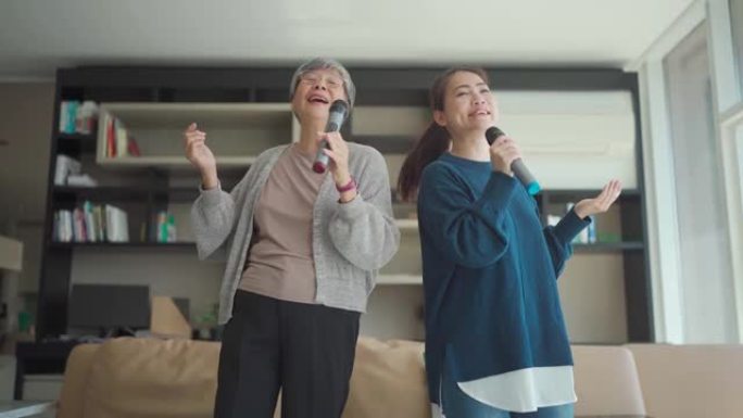 亚洲华裔高级女子在周末休闲活动中与女儿在客厅唱歌卡拉ok跳舞