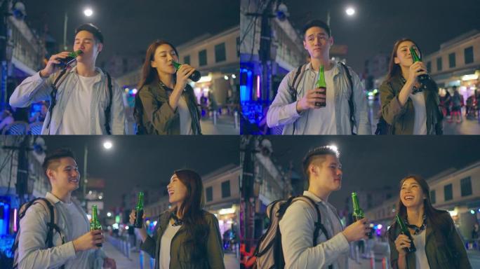 亚洲迷人的夫妇喝酒，一起开派对。在城市旅行的年轻男女游客在旅途中度过假期，在漆黑的夜晚一起拿着一瓶啤