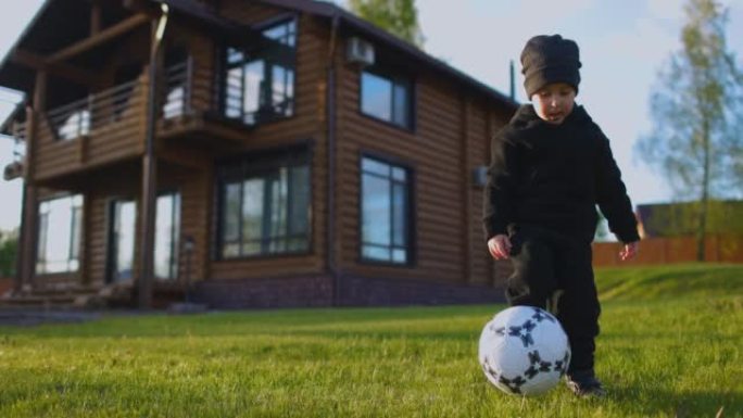 一个小男孩在房子后面的田野里用脚踢足球