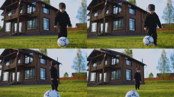 一个小男孩在房子后面的田野里用脚踢足球