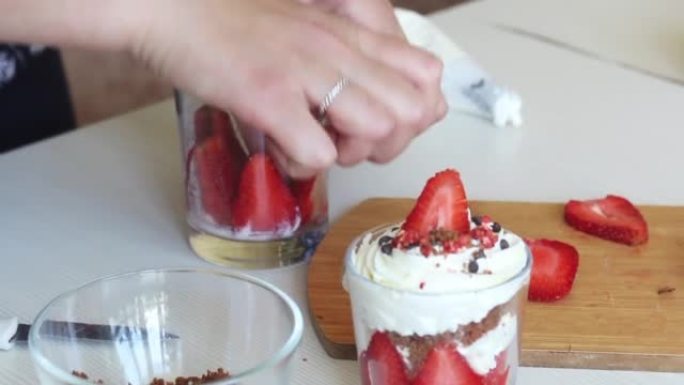 一个女人用草莓，鲜奶油和脆饼准备甜点。装饰有巧克力滴和冻干草莓。特写。