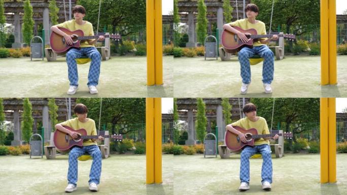 十几岁的男孩独自无聊地坐在秋千上摇摆在操场上弹吉他