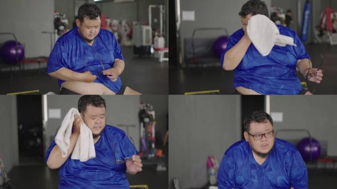 超重男子在健身房休息时清洁眼镜擦去汗水。