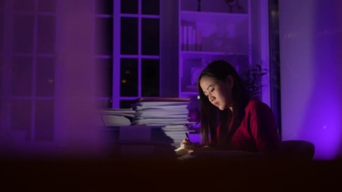 紧张的年轻亚洲妇女坐在办公室加班加班，晚上在办公桌上做深夜生意，疲惫的女商人概念。