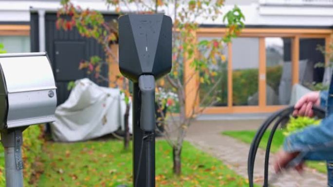 私人停车场家庭从充电箱中卷绕电动汽车充电电缆的特写视图。瑞典。