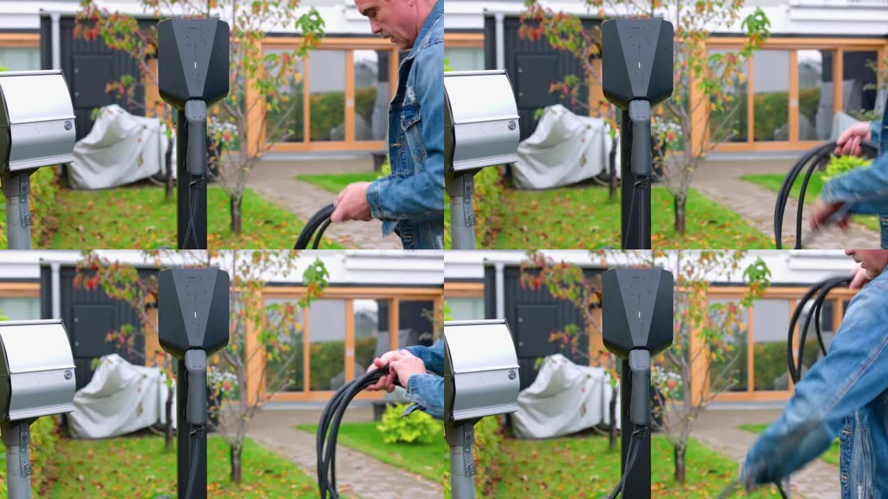 私人停车场家庭从充电箱中卷绕电动汽车充电电缆的特写视图。瑞典。