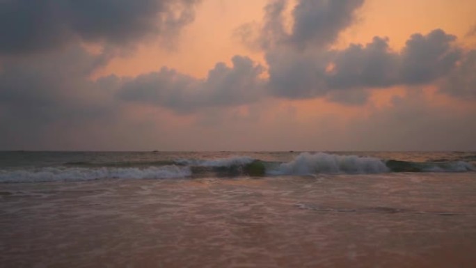 在印度果阿的北果阿，日落期间，巴加海滩的广角慢动作拍摄，海洋上空有云彩。日落后，海面上的云波与戏剧性