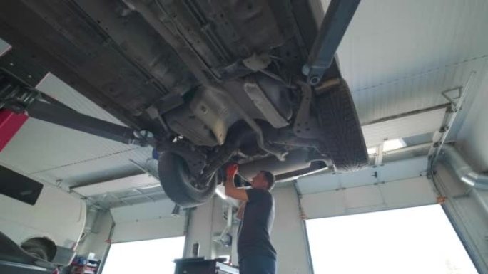 年轻的专业机械师在汽车维修服务的现代汽车下工作。汽车服务，维修保养。
