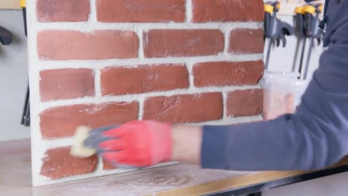 防护橡胶手套的工人用湿海绵擦拭仿制的砖砌元件，将其从建筑灰尘中清除。基于旧砖铸件的瓷砖制成的饰面材料