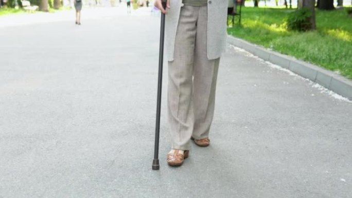 关闭在公园里用拐杖走路的高级女性腿。老年女性，在公园享受阳光明媚的日子，养老金娱乐