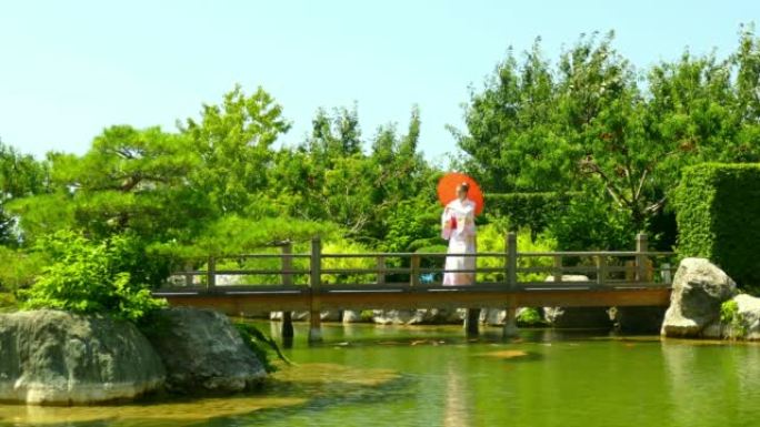 穿着和服，在公园里的池塘桥上拿着雨伞的年轻女子