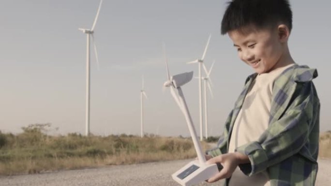在风电场手握玩具风车的快乐亚洲孩子，可再生能源概念