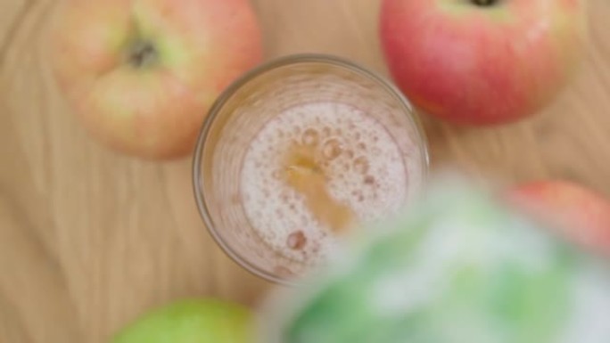 将苹果汁倒入玻璃杯中。成熟的苹果躺在桌子上。选择性聚焦。慢动作