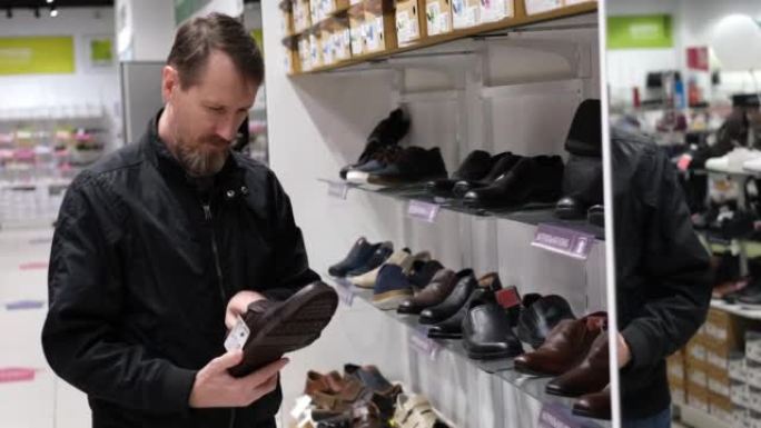 男士购物者在商店里选择鞋子，检查质量并考虑购买。慢动作。货架上有俄罗斯真皮鞋标签的铭文