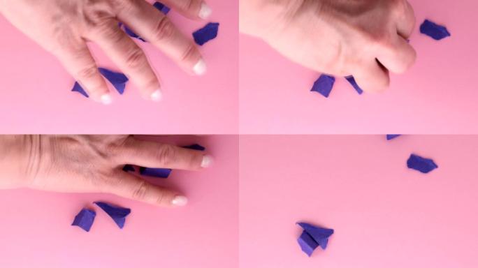 4k视频，一个女人的手从桌子上取下粉红色背景上的皱巴巴的紫色纸片，顶视图