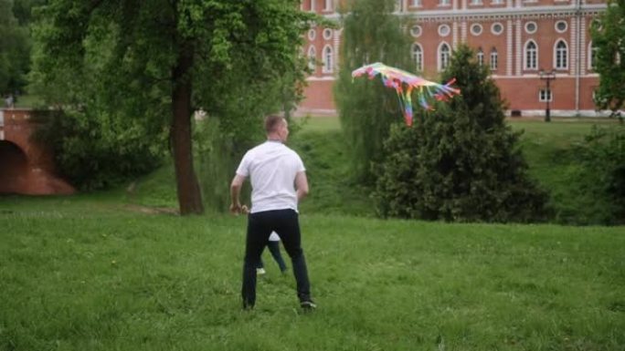 男子在绿地上的公园里放风筝，一家人追赶他