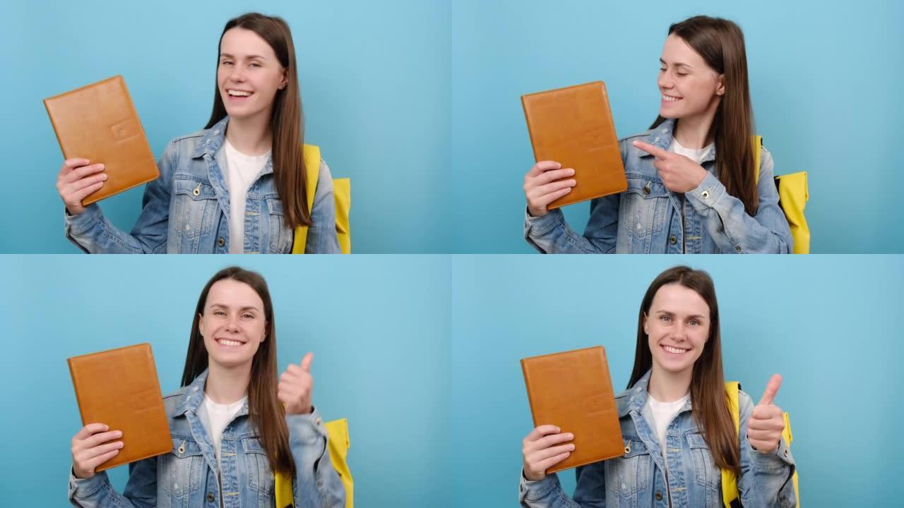 肖像快乐女孩青少年学生用手指指着书，露出拇指，穿着黄色背包，在工作室里孤立在蓝色背景上。高中教育大学