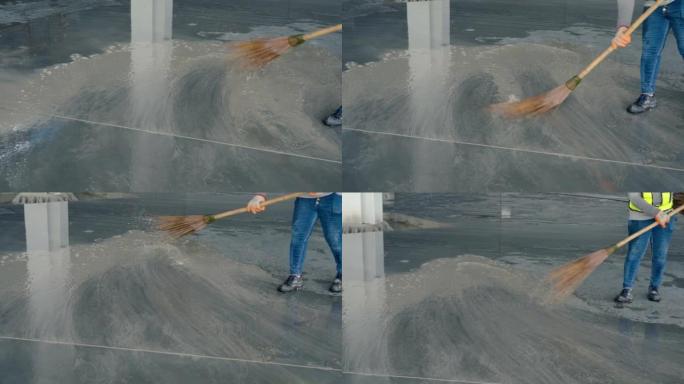 4K，使用扫帚在建筑工人的脚下射击。扫地清洁水泥地板，这是施工现场工作的脏水。