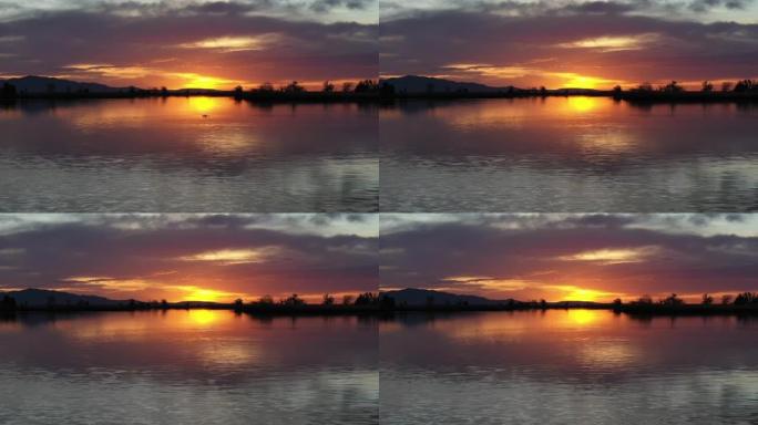 日落时的湖泊，阴天的日落反射在水面上，一条鱼跳出水面
