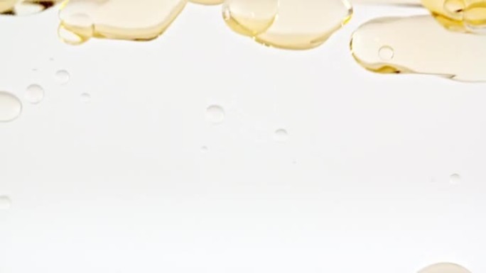移动的黄色金色油的慢动作，浅白色背景上的水中气泡上升。带有气泡的透明化妆品凝胶液。宏观拍摄。