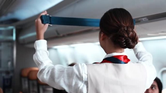 亚洲美女空姐在飞机起飞前关闭头顶的行李架，检查乘客和飞机内人群的安全。航空公司的概念。