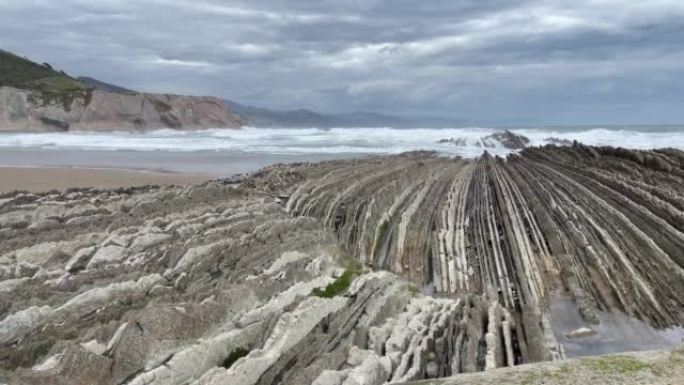 汹涌的海浪在Zumaia海滩的尖锐石灰岩岩层上破裂