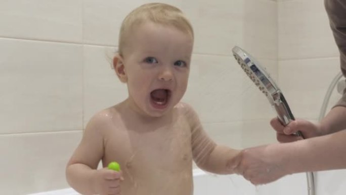 快乐的孩子在浴室洗澡时笑，母亲给她一岁的婴儿倒水。健康、儿童发展和家庭乐趣的概念。
