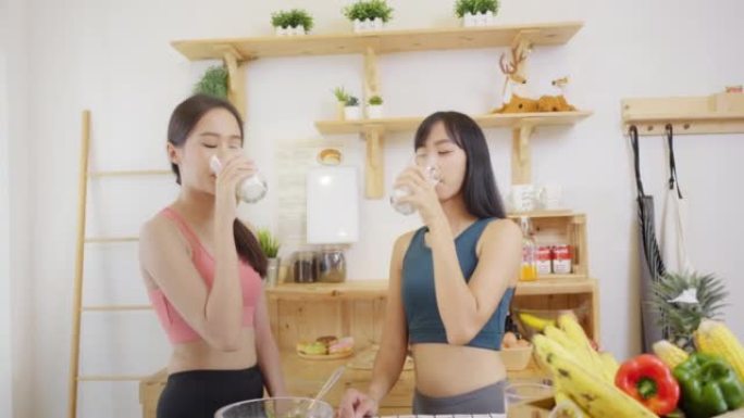 照顾健康的亚洲妇女穿着运动服，站在厨房喝牛奶