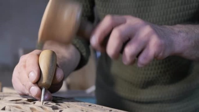 木雕大师的男性手拿着木锤和锋利的锥子，用木柄敲击木板上的图案。爱好和工艺