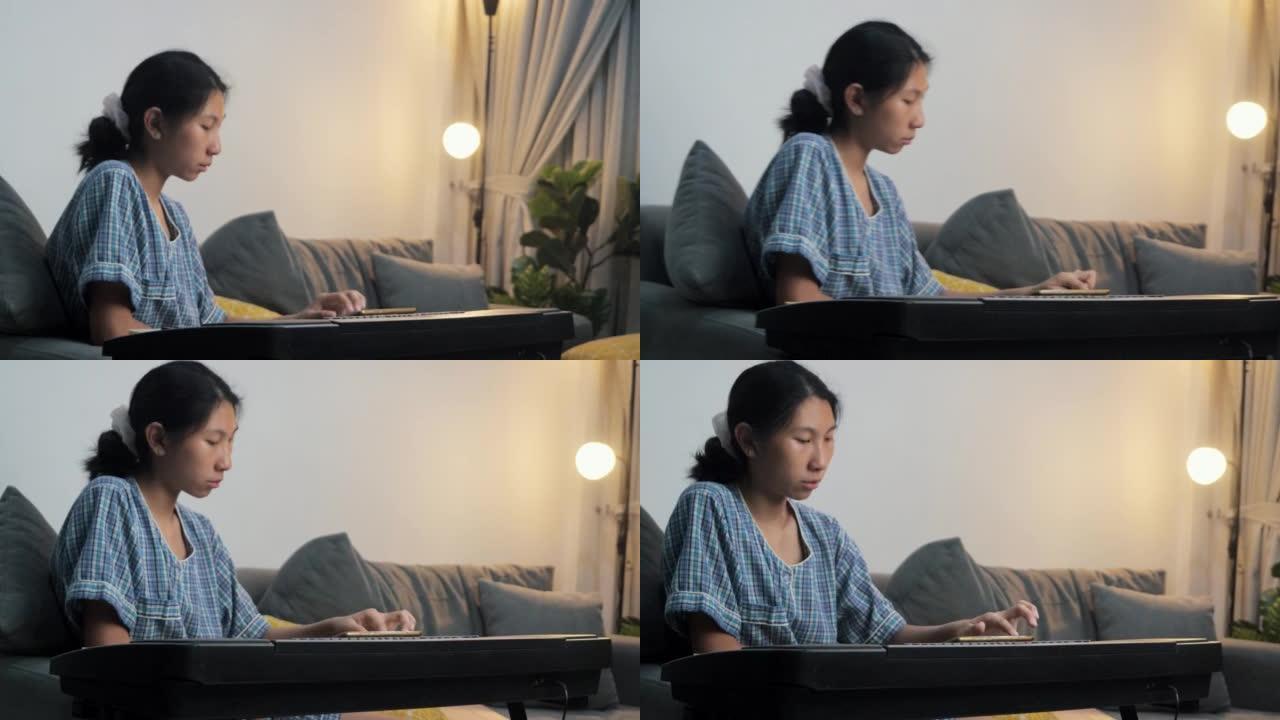 穿着睡衣的亚洲女孩在晚上在家的沙发上通过移动应用学习弹奏键盘乐器，生活方式概念。