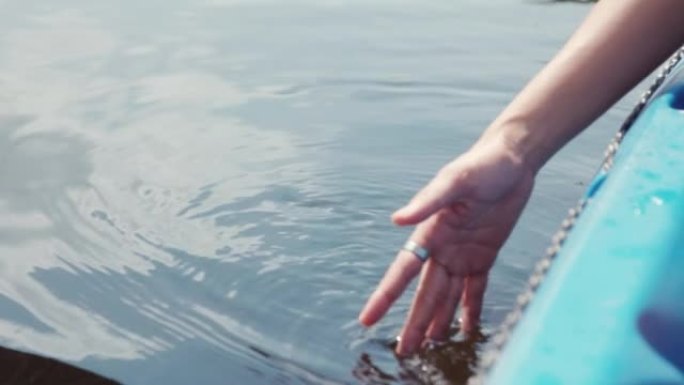 年轻女子的近手，在湖中阳光照射下触碰水和水反射。它展示了暑假与大自然放松和平静的概念。
