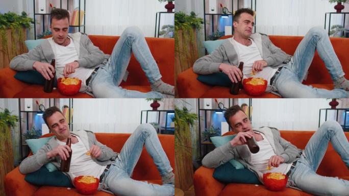 男人坐在沙发上吃薯条，在家看有趣的电视连续剧，在线足球比赛