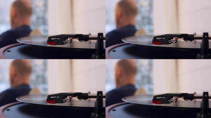 在转盘中旋转的黑胶唱片的特写镜头。在模糊的背景中，一个无法识别的人正在听音乐。一个听音乐的男人在家里