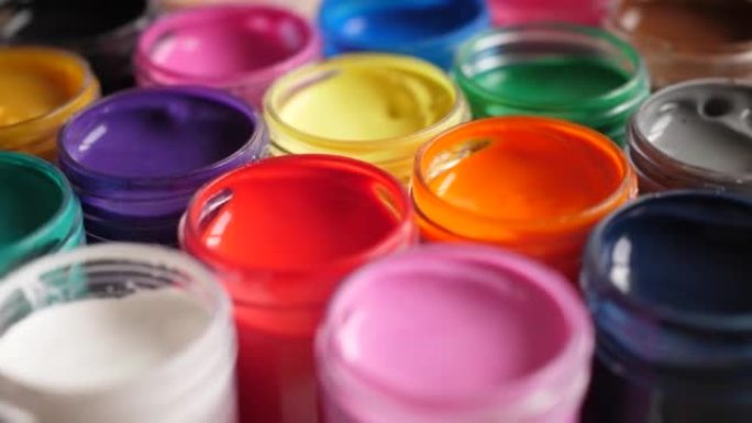 将水粉画颜料放在罐子里明亮的颜色特写。塑料罐上的多色水粉旋转套装。旋转多色背景。多色油漆的背景。创意