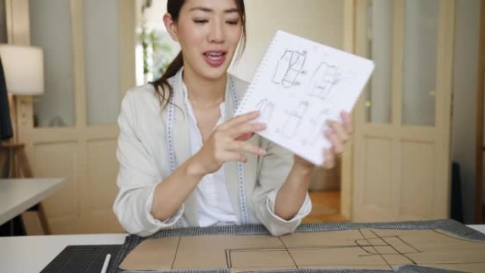 女性时装裁缝，日本人看着相机并在素描本上展示她的设计图