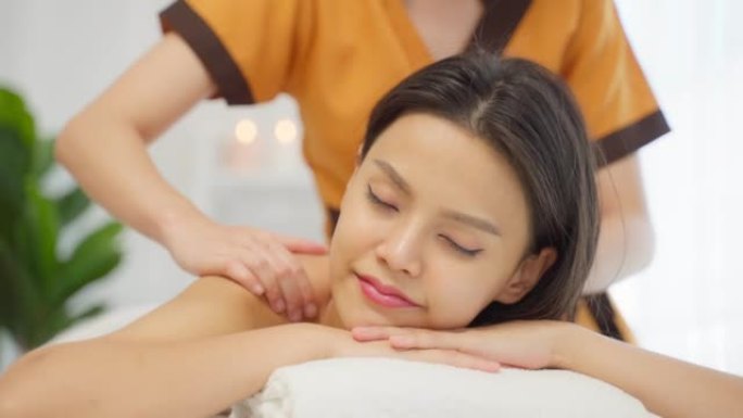 亚洲年轻女子在用油按摩背部时感到快乐和放松。美丽迷人的女孩躺在按摩台上，在水疗美容院接受按摩师的皮肤