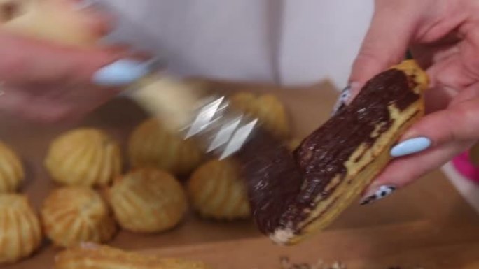 一个女人用巧克力涂抹蛋糕，然后将其浸入坚果中。自制奶油泡芙放在盘子里。糕点。中等计划。
