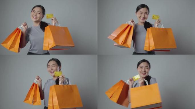 亚洲女人开心地微笑着拿着购物袋，挥舞着信用卡看着相机。