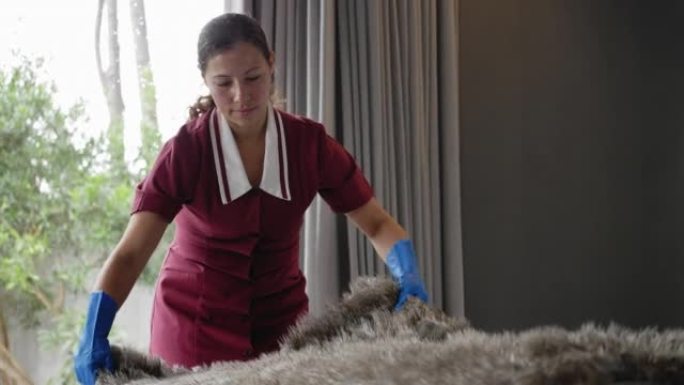 戴着手套的女佣在酒店房间的床上整理毯子