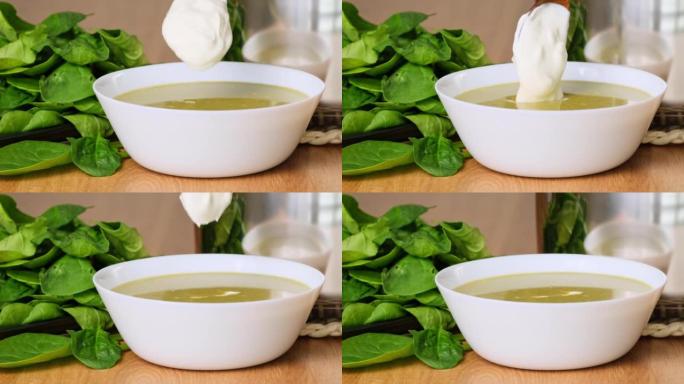 一碗健康的绿色菠菜汤配奶油。厨师用奶油装饰菠菜或西兰花汤。菠菜奶油汤。在汤特写中加入酸奶油