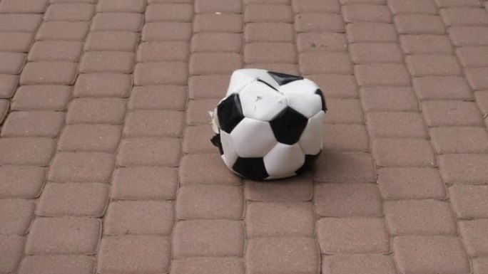 有划痕、部分漏气的足球破损躺在铺着瓷砖的路面上