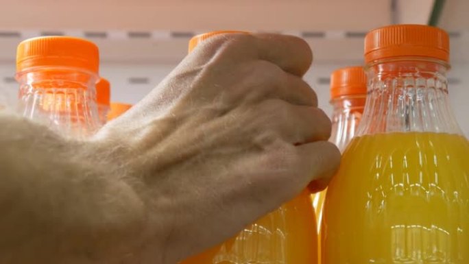 许多带有不同柑橘汁的塑料瓶的特写镜头，一只男性的手拿了一个
