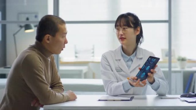 亚洲女医生向患者展示平板电脑上的x射线