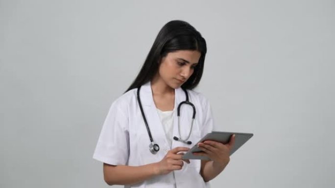 穿着白色制服和听诊器的年轻印度医生。观看ipod平板电脑。