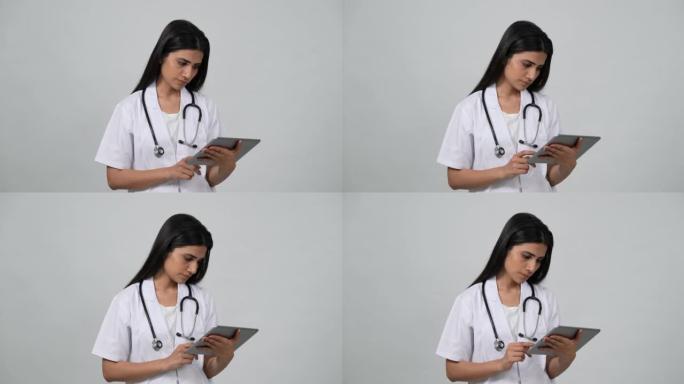 穿着白色制服和听诊器的年轻印度医生。观看ipod平板电脑。