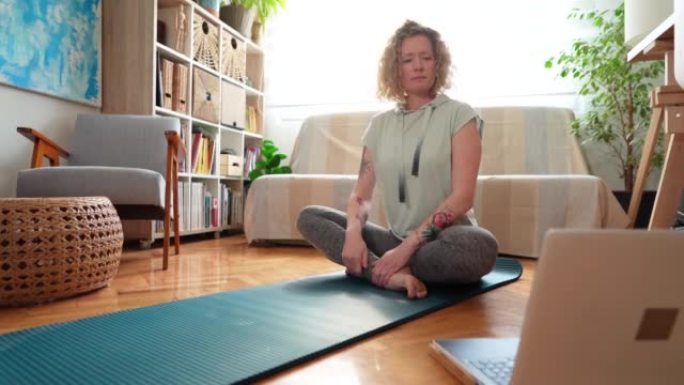 白人妇女在笔记本电脑上进行在线瑜伽课，同时在家锻炼