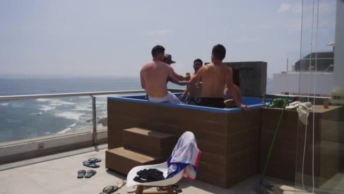 几个朋友在4k阳光明媚的日子里，在海滨别墅露台上的游泳池里敬酒喝啤酒和葡萄酒，背景是大海